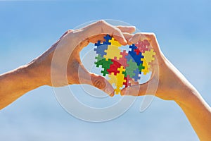 Child and adult hands holding colorful heart on blue sky background. World autism awareness day concept