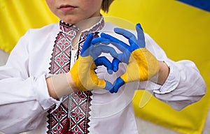 Child against the background of the Ukrainian flag with hands in the shape of a heart, painted in yellow and blue