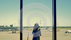 A child in the airport. A boy looks at the airport runway through the window.