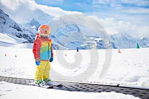 Child in alpine ski school with magic carpet lift and colorful training cones going downhill in the mountains on a sunny winter