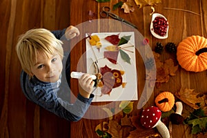 Child, applying leaves using glue, scissors, and paint, while doing arts and crafts at home