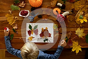 Child, applying leaves using glue, scissors, and paint, while doing arts and crafts at home