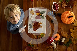 Child, applying leaves using glue, scissors, and paint, while doing arts and crafts at home