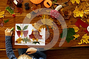 Child, applying leaves using glue, scissors, and paint, while doing arts and crafts at home