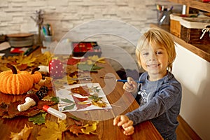 Child, applying leaves using glue, scissors, and paint, while doing arts and crafts at home