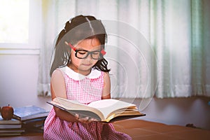 Child asian little girl put on eyeglasses reading a book