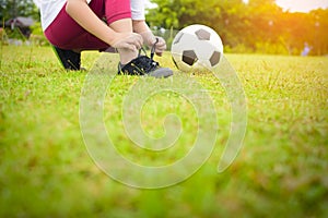 Child Asian tying shoes with ball on green grass.