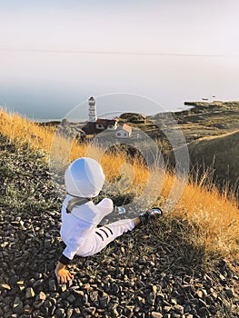 Child in astronaut costume relaxing on hill