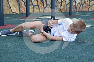 Child athlete fell to the ground. sports injury of a child`s leg.