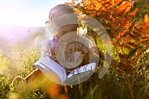 The child in the autumn. A girl with a book is sitting on the grass in the sun at sunset.