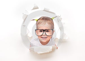 Child baby girl with funny tails with glasses peeping through a hole in white paper