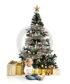 Child baby girl kid sitting under decorated gold Christmas tree with gold patchwork gift