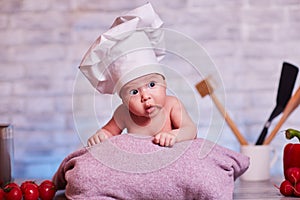 Child, baby girl lies on the kitchen table in a chef`s cap - next to him are vegetables, bell pepper, radish, broccoli, proper