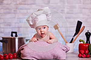 Child, baby girl lies on the kitchen table in a chef`s cap - next to him are vegetables, bell pepper, radish, broccoli, proper