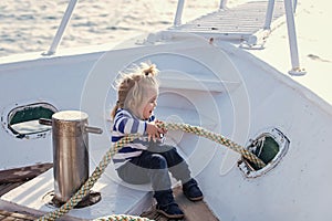 Child baby playing with rope on yacht. Little child sitting and berthing rope on white boat. Travel and summer vacations