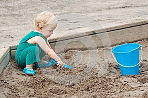 Child baby in sandbox playing with beach toys. Girl toddler digging sand and building sandpie. Kid have fun on playground. Summer