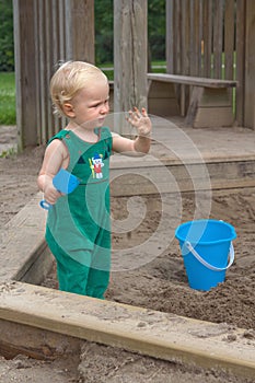 Child baby in sandbox playing with beach toys. Girl toddler watching exploring sand on hands. Kid have fun on playground. Summer