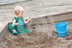 Child baby in sandbox playing with beach toys. Girl toddler watching exploring sand on hands. Kid have fun on playground. Summer