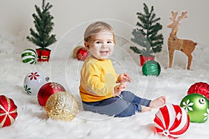 Child baby in yellow sweater clothes sitting on white fluffy rug celebrating Christmas or New Year