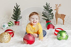 Child baby in yellow sweater clothes sitting on white fluffy rug celebrating Christmas or New Year