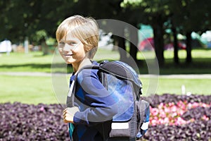 Child with a backpack go to school. City park background