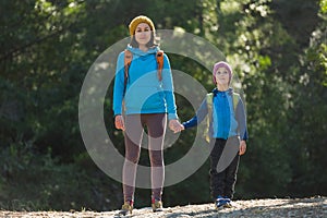 A child with a backpack walks in the forest with his mother