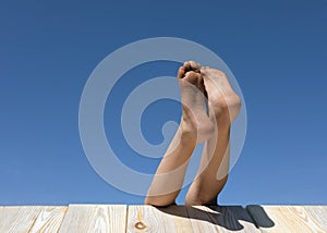 Child bare legs protrude from table on blue sky background. photo