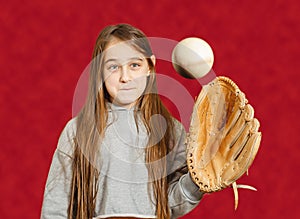 A child with a baseball glove and a ball. A girl with long hair catches a baseball with a baseball glove. Red background