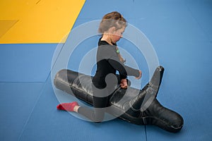 The child beats the training dummy with his hands. A little girl sits on top on a training mannequin and works off punches.