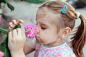 Little girl with flowers, portrait near a blooming rose bush, close-up, horizontal shot. summer time. Summer time