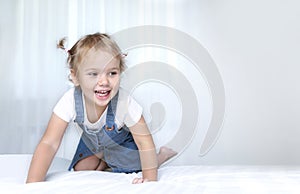 Child on a bed empty copy space background.Girl in white sheet in bedroom.Happy kid jumping on bed