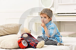 Child in bedroom with silence gesture. Boy with calm face puts favourite toy on bed, time to sleep. Kid put plush bear