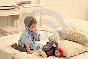 Child in bedroom with silence gesture. Time to sleep concept. Boy with happy face puts favourite toy on bed, time to