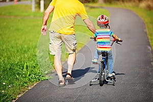 A child on a bicycle in helmet with father on asphalt road