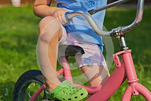 A child on a bicycle with an injured knee,a little girl is sitting on a bicycle with a bruised knee