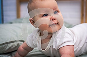 A child with big blue eyes lies on his tummy with an interested look