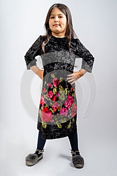 A child in a black corduroy dress with flower patterns, blue tights and grey shoes isolated on a white background.
