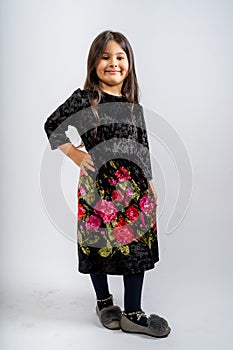 A child in a black corduroy dress with flower patterns, blue tights and grey shoes isolated on a white background.