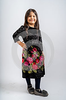 A child in a black corduroy dress with flower patterns, blue tights and grey shoes isolated on a white background. photo