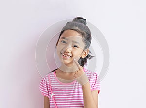 The child with black hair is smiling and pointing to her face