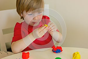 child blond boy playing with plasticine while sitting at table. childhood, developing activities for children