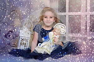 Child blonde in a blue dress sitting on the bed with a flashlight and a Russian New Year`s doll in a kokoshnik