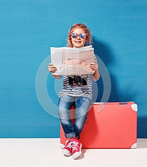Child blonde girl with pink vintage suitcase and city map ready for summer vacation. Travel and adventure concept