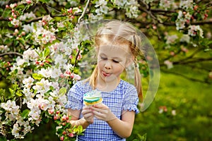 A child in a blooming apple orchard enjoys a warm spring day. The girl holds a cake in her hands, wants to eat it