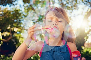 Child, blowing and bubbles in garden or playing in summer sunshine in backyard for holiday, carefree or happy. Kid, girl