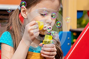 Child blowing soap bubbles in summer on sunny day in the playground