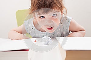 The child blows on a ball of paper at the table.