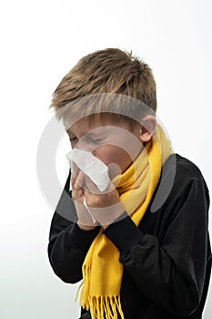 A child blows his nose into a napkin, children's seasonal diseases, a boy wrapped in a scarf.