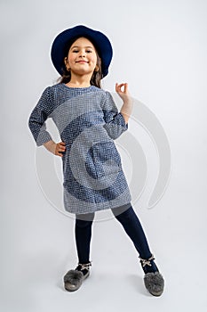 A child in a blue dress with white and black spots, a blue hat, blue tights and gray shoes isolated on a white background.