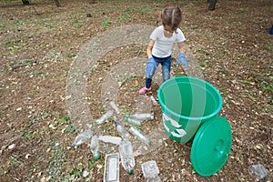 Child in blue latex gloves, throwing plastic bag into recycling bin. Land and rubbish on the background, outside photo,